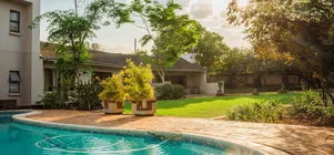 Swimming pool with surrounding garden and buildings in a sunny outdoor setting