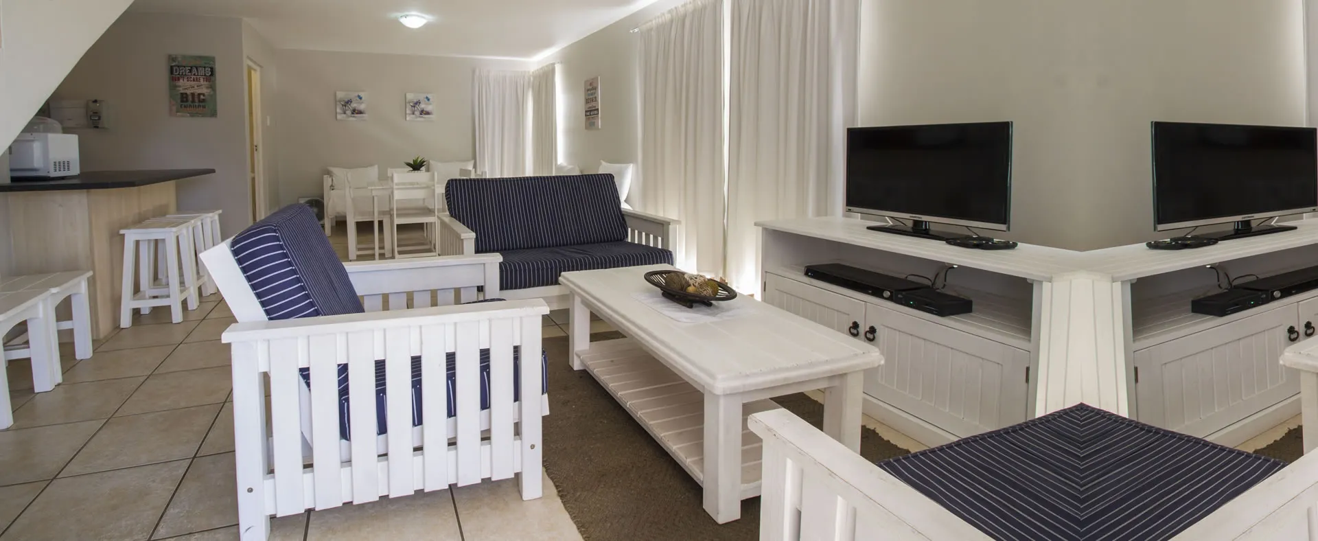 Modern living room with white furniture blue cushions and two flatscreen TVs
