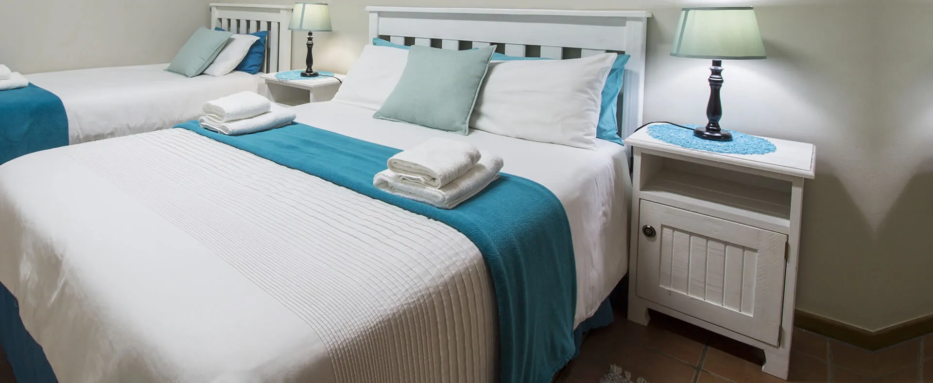 Two neatly made beds in a bedroom with white and teal bedding