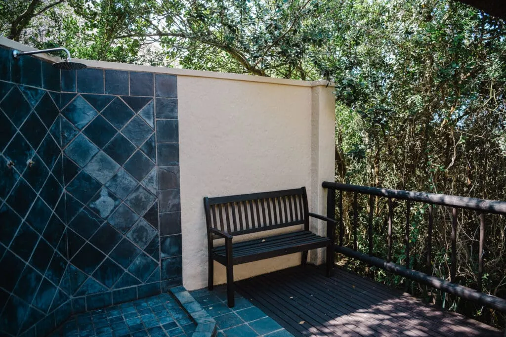 Outdoor bench next to tiled wall on a wooden deck with greenery background