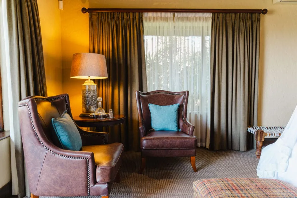 Two brown armchairs in a cozy room with curtains and a lamp