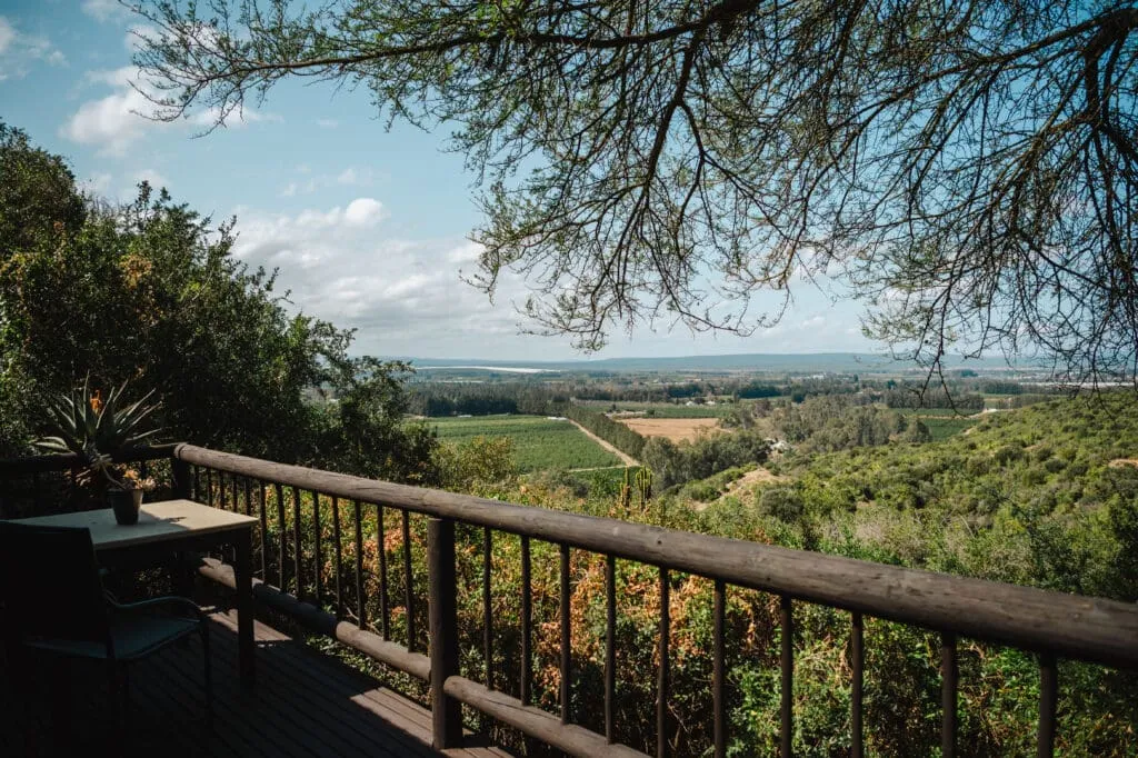 Wooden deck with railing overlooking a lush valley and distant fields