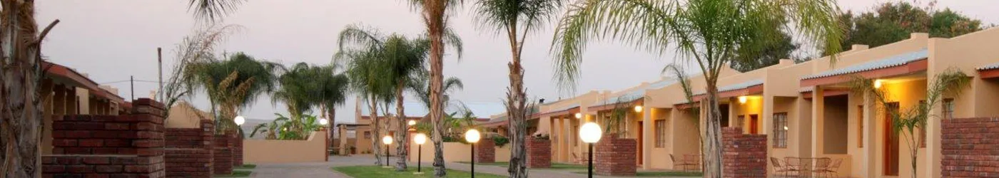 Row of singlestory buildings with palm trees and street lamps at dusk