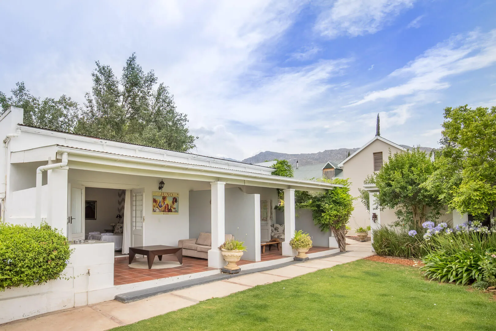 White house with veranda potted plants and green lawn under a blue sky