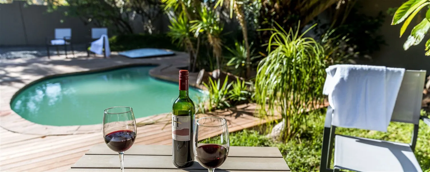 Wine bottle and glasses on a table by a pool with lounge chairs