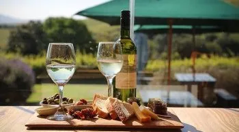 Two wine glasses a bottle and a charcuterie board on a wooden table outdoors