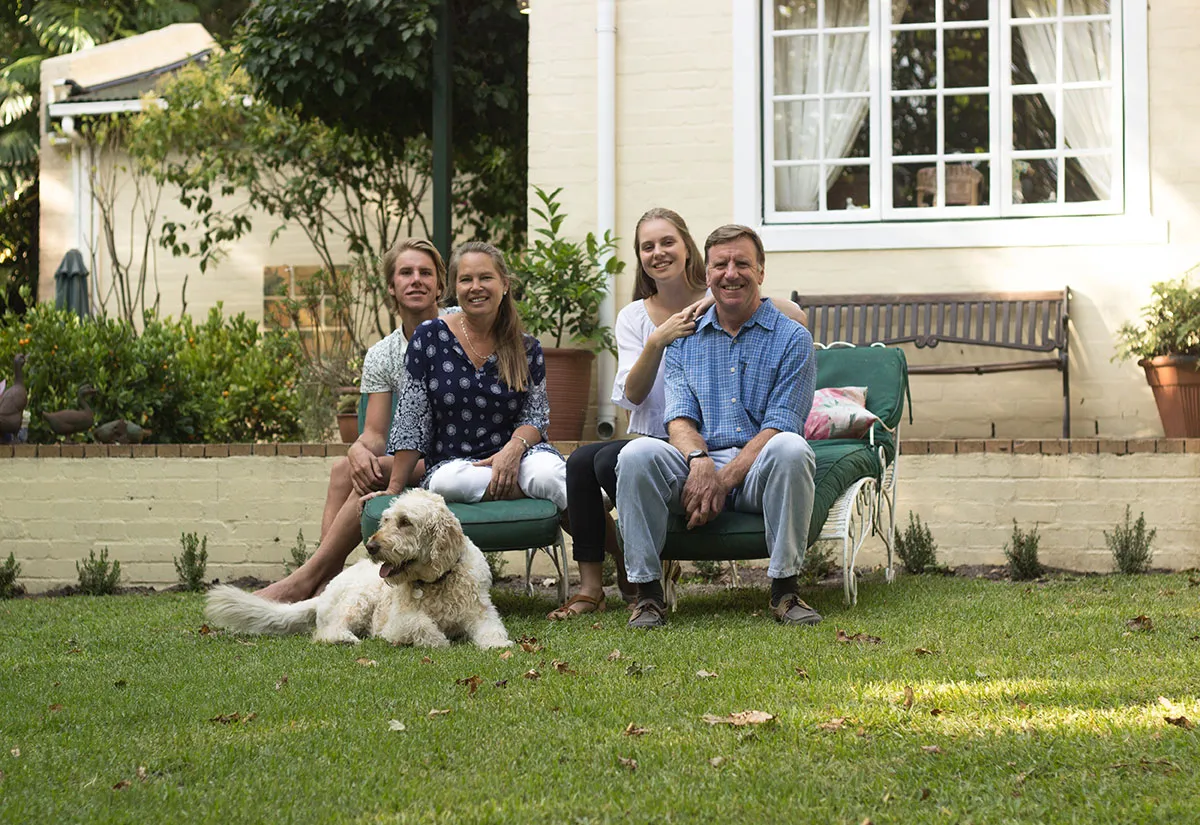 Family sitting on a bench in a garden with a dog on the grass