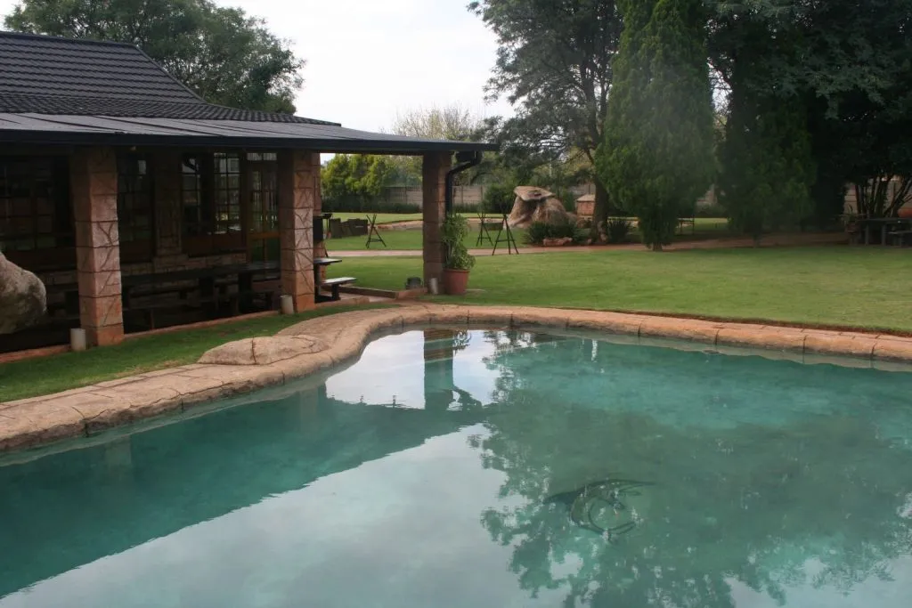 Swimming pool in a garden with a house and trees in the background