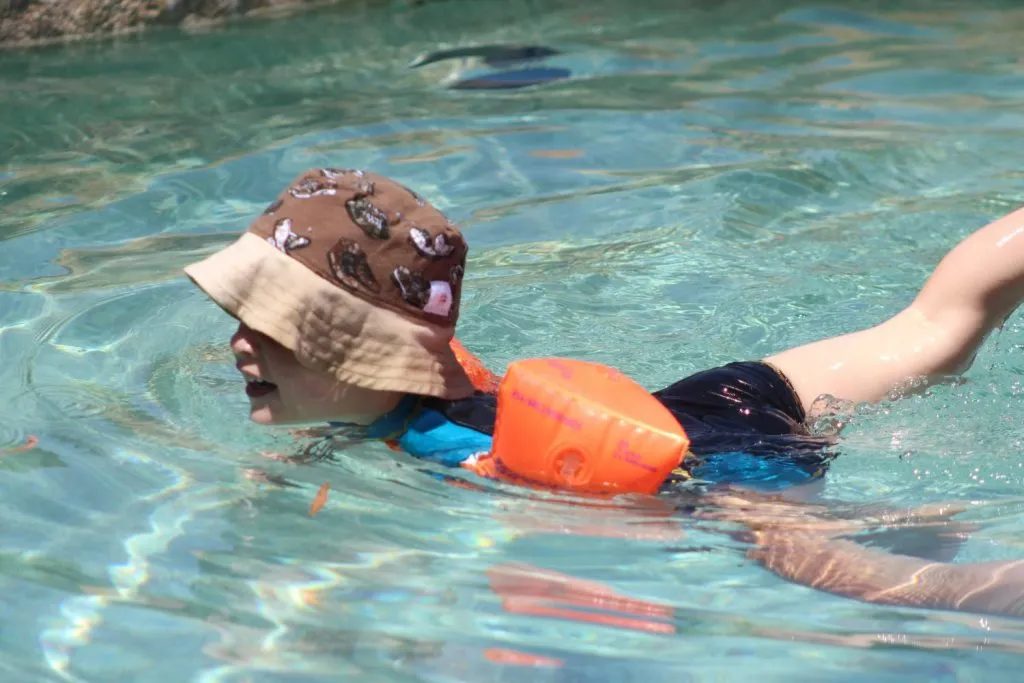 Child swimming in a pool wearing a hat and inflatable armbands