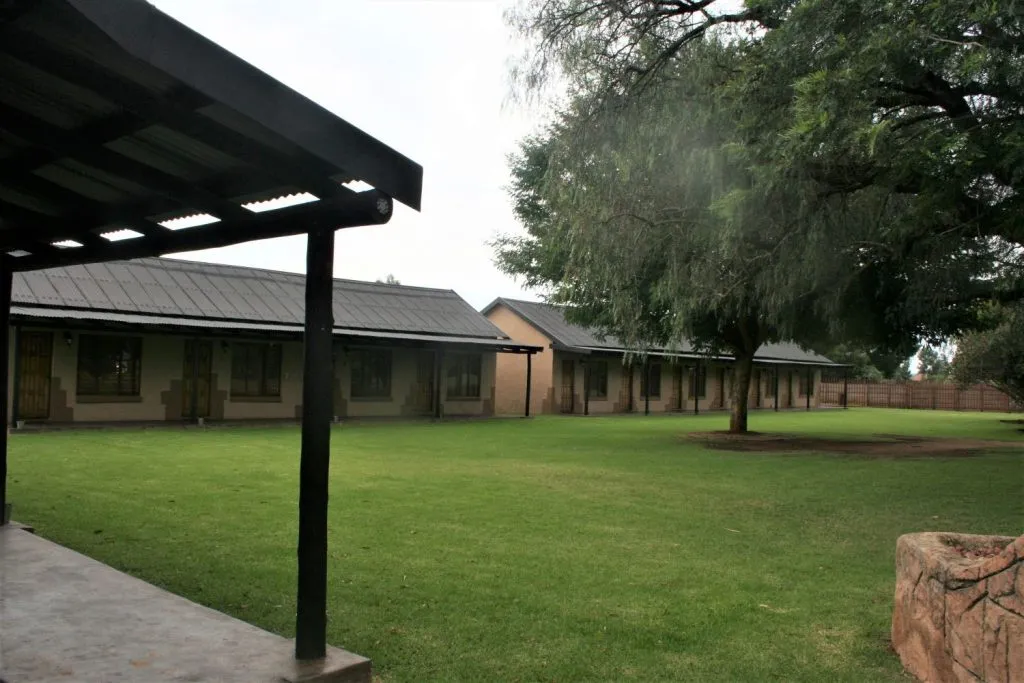 Row of singlestory buildings with a green lawn and large tree in front