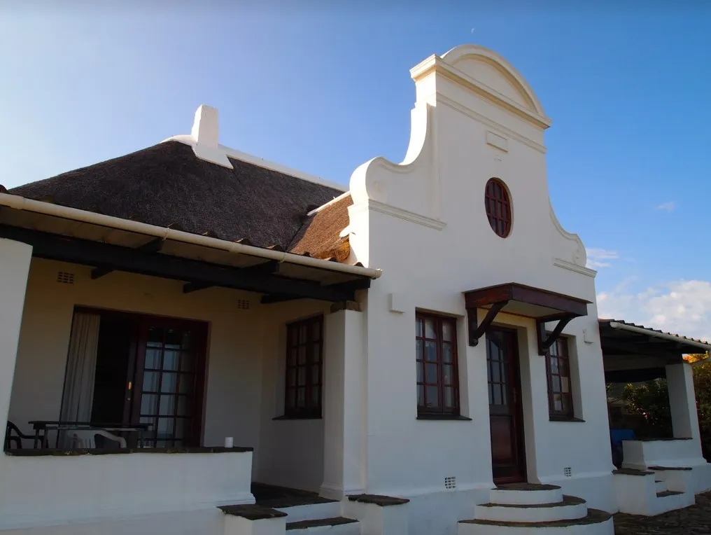 White traditional house with a thatched roof and wooden windows under a blue sky