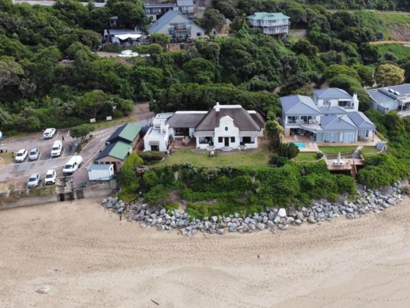 Aerial view of beachfront houses surrounded by greenery and parked cars