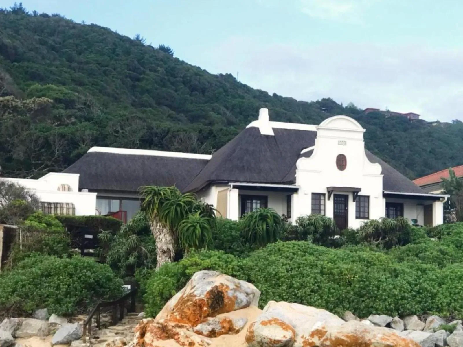 Large house with a thatched roof surrounded by greenery and rocks