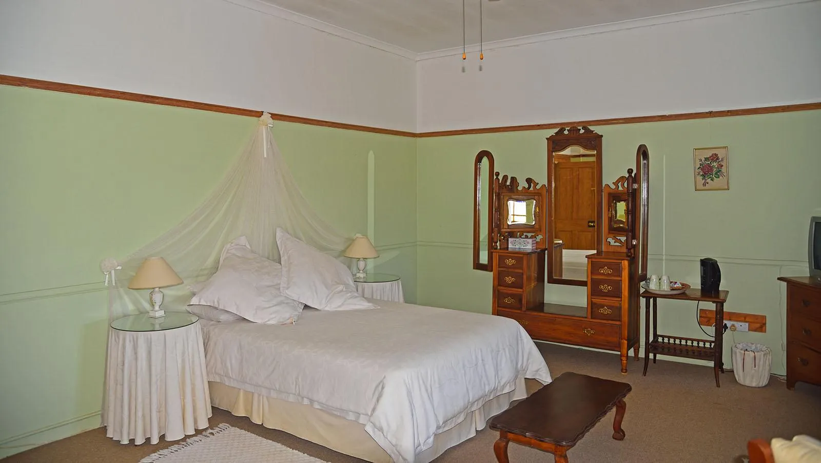 Bedroom with a white bed wooden dresser and green walls