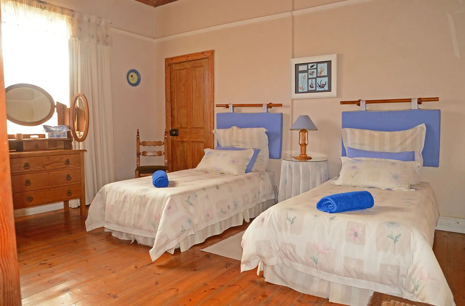Two single beds in a tidy bedroom with wooden floor and furniture
