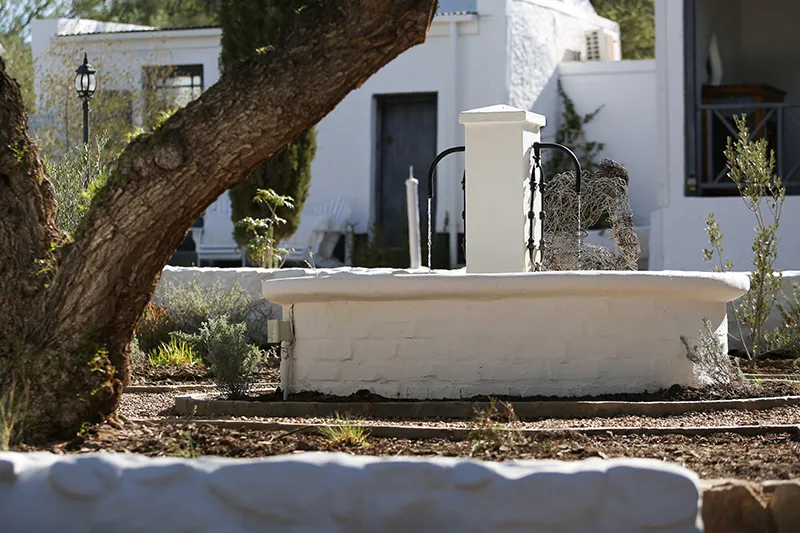 Outdoor water pump with white brick base near a tree and white building