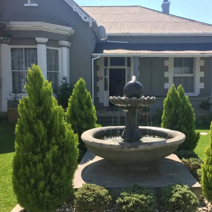 A fountain in front of a gray house with white trim and windows