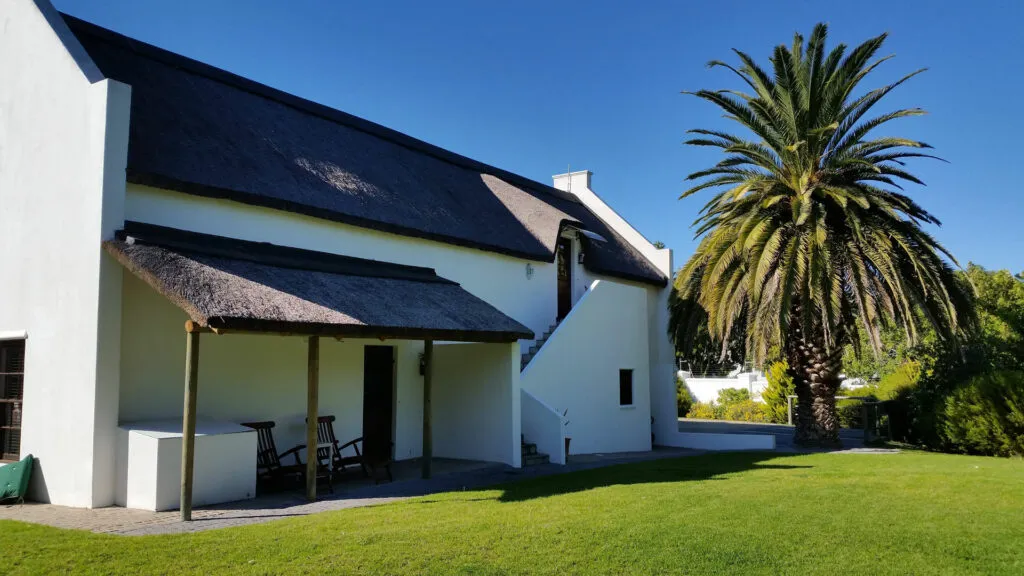 White house with thatched roof and palm tree in a green lawn