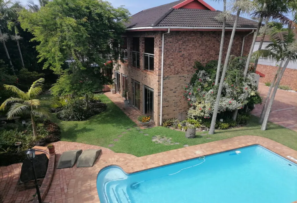Twostory brick house with pool garden and palm trees in sunny weather