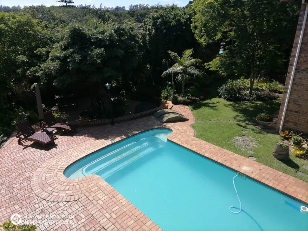 Swimming pool surrounded by greenery and brick patio in a garden setting