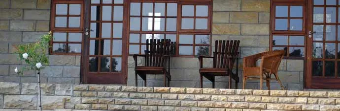 Three wooden chairs on a stone patio with large windows in the background