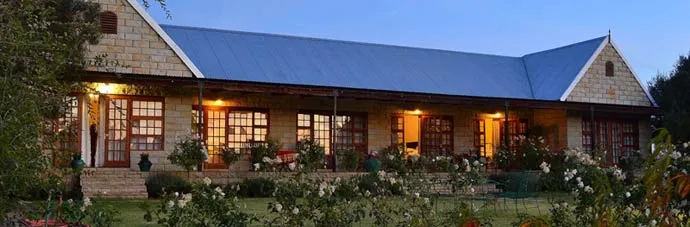 Country house with stone walls and blue roof surrounded by flowers at dusk