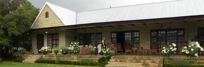 Large house with veranda white roof and people sitting outside in garden setting