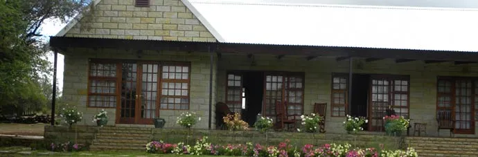 Stone house with large windows wooden doors and a flower garden in front