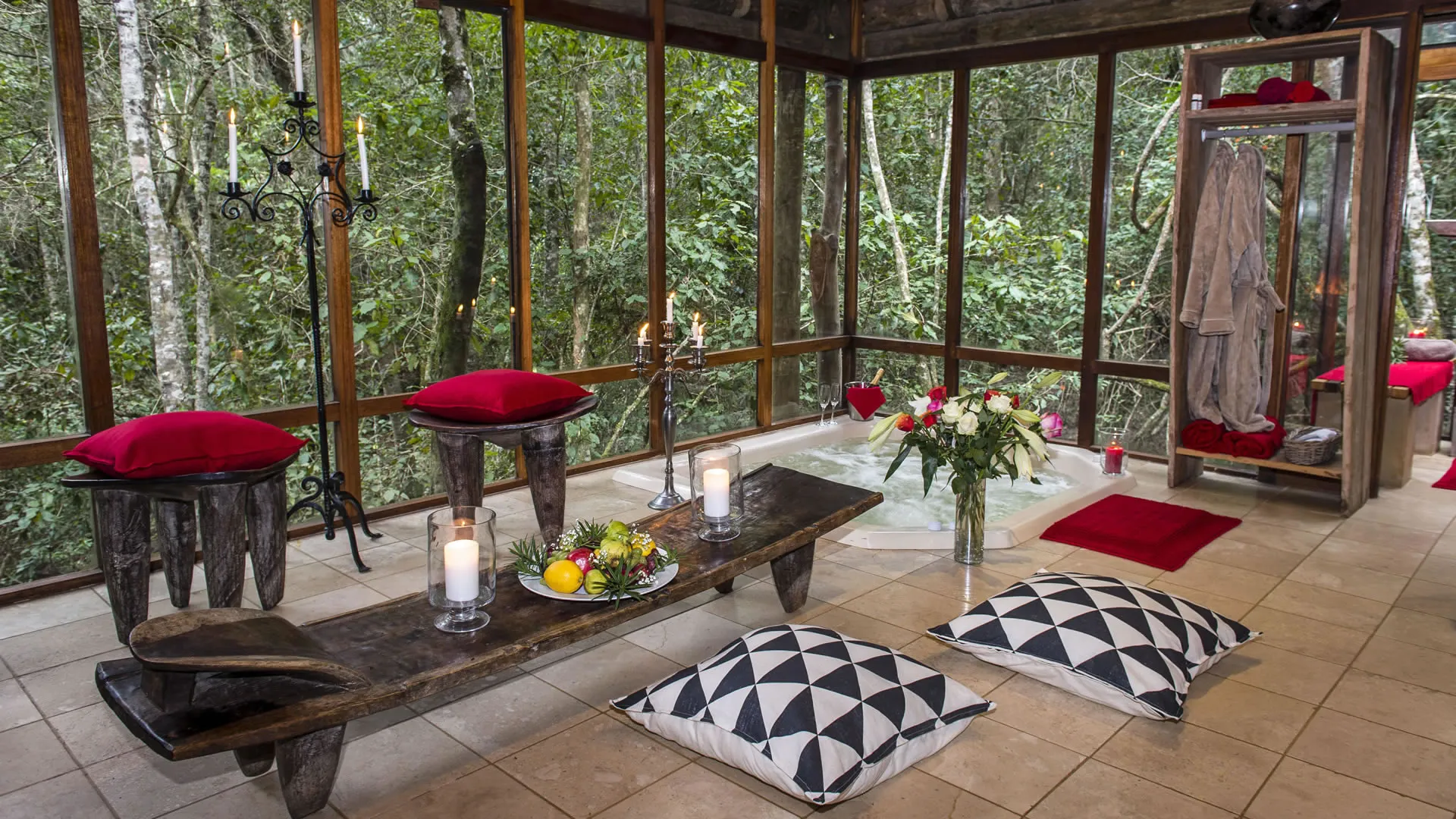Wooden bench with candles and fruit surrounded by large windows and forest view