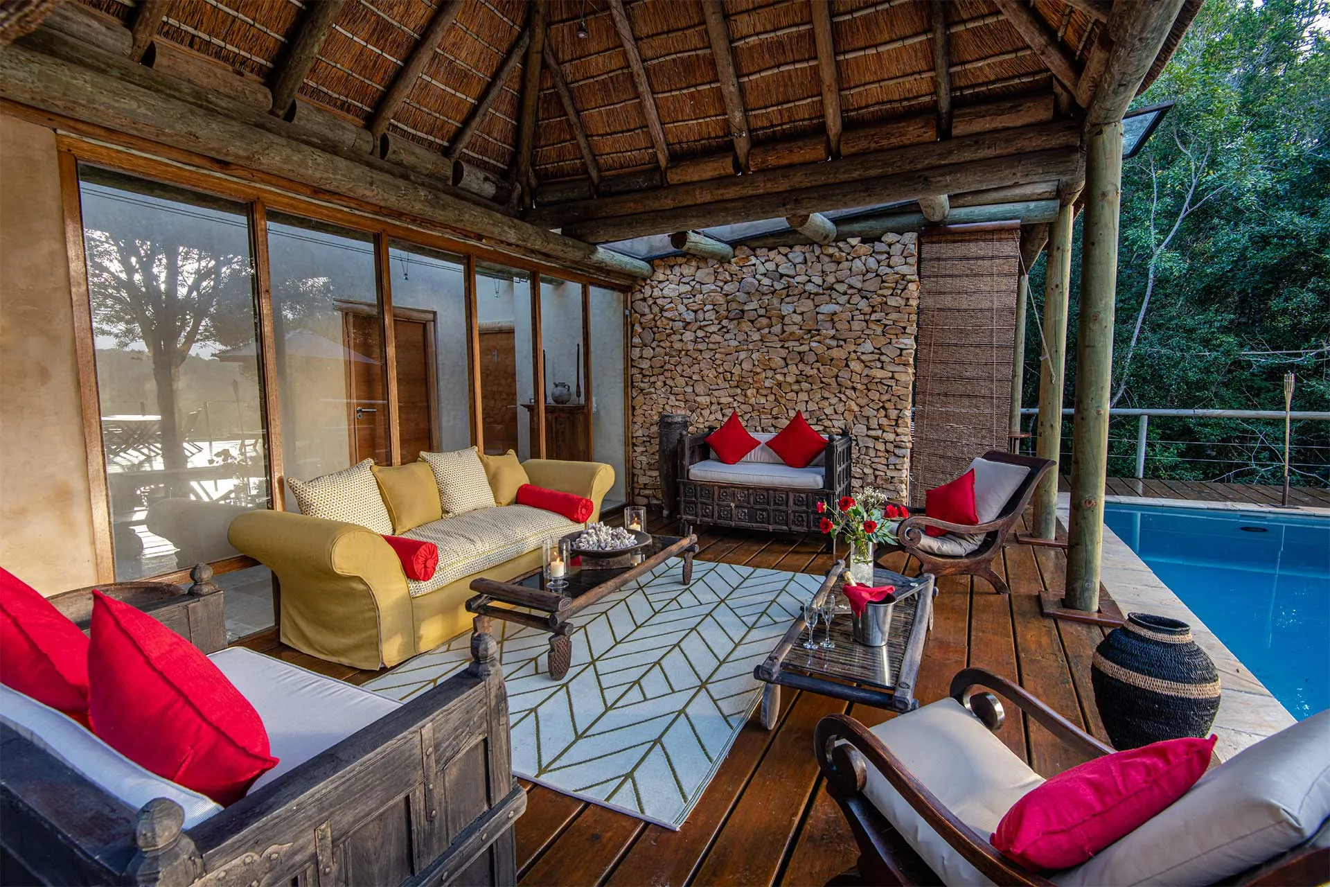 Wooden patio with yellow and white furniture red cushions and a stone wall backdrop