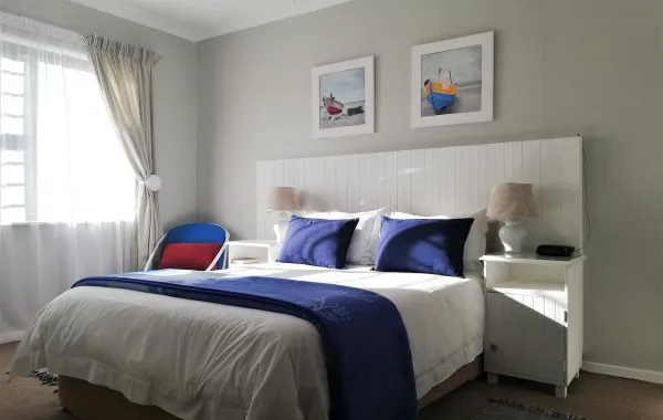 Bright bedroom with white bed blue bedding and nautical artwork on the wall