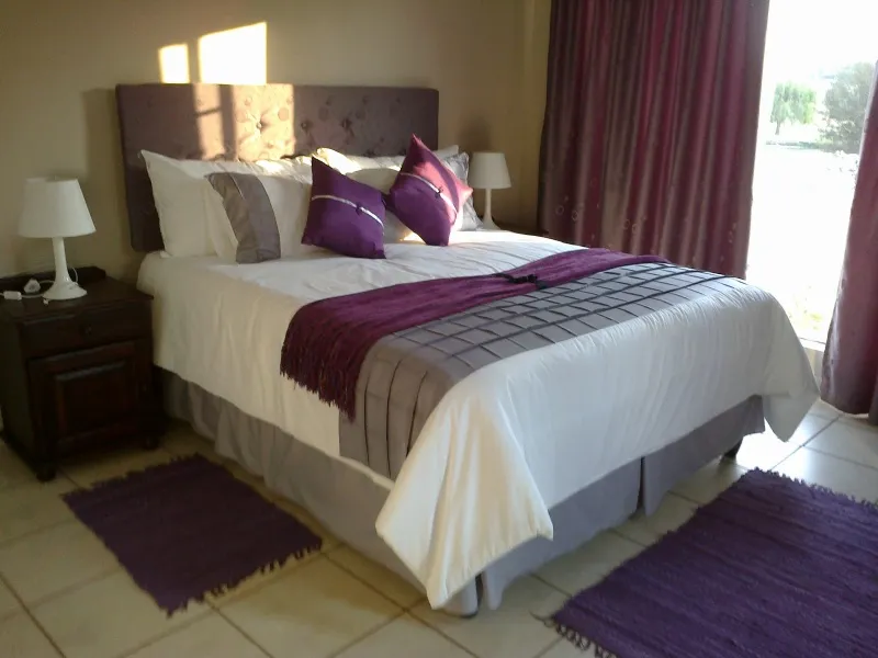 Bedroom with a large bed purple and grey bedding and matching rugs