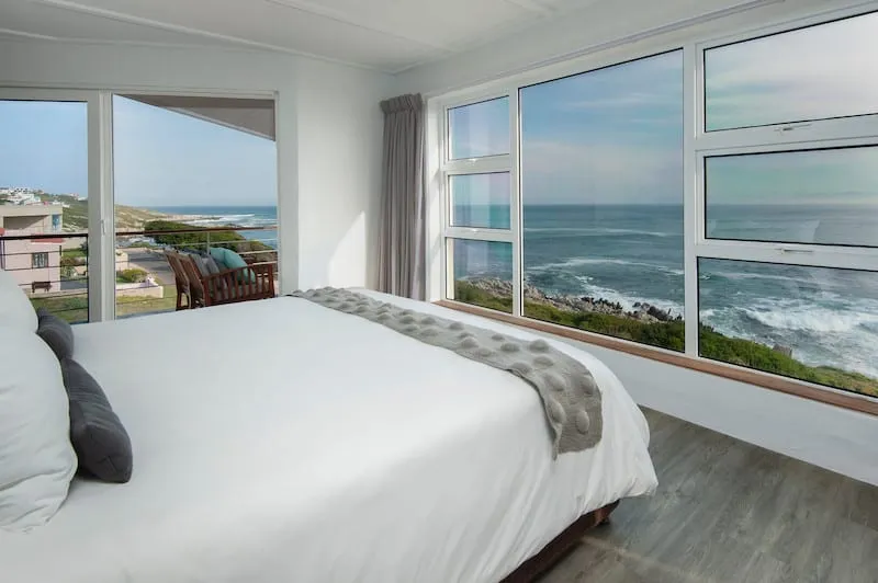 Bedroom with large windows overlooking the ocean white bedding and wooden floor