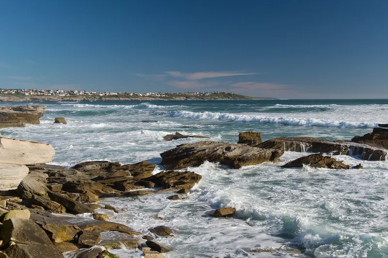 Rocky coastline with waves crashing against rocks under a clear blue sky