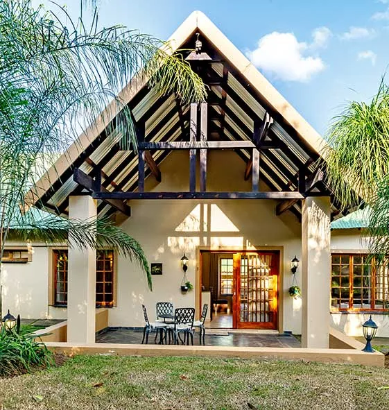 Chalet with a peaked roof surrounded by palm trees and grass