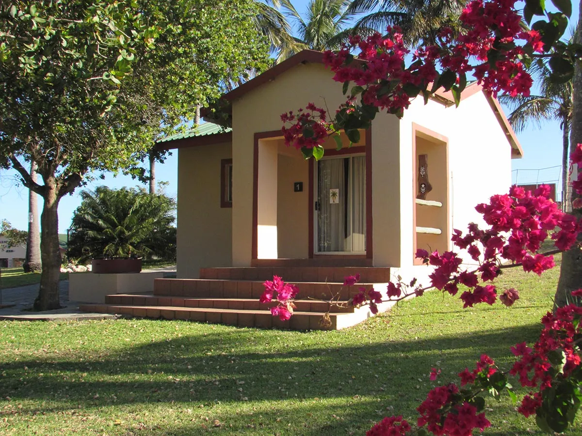 Small beige cottage with red flowers and green trees in a garden setting