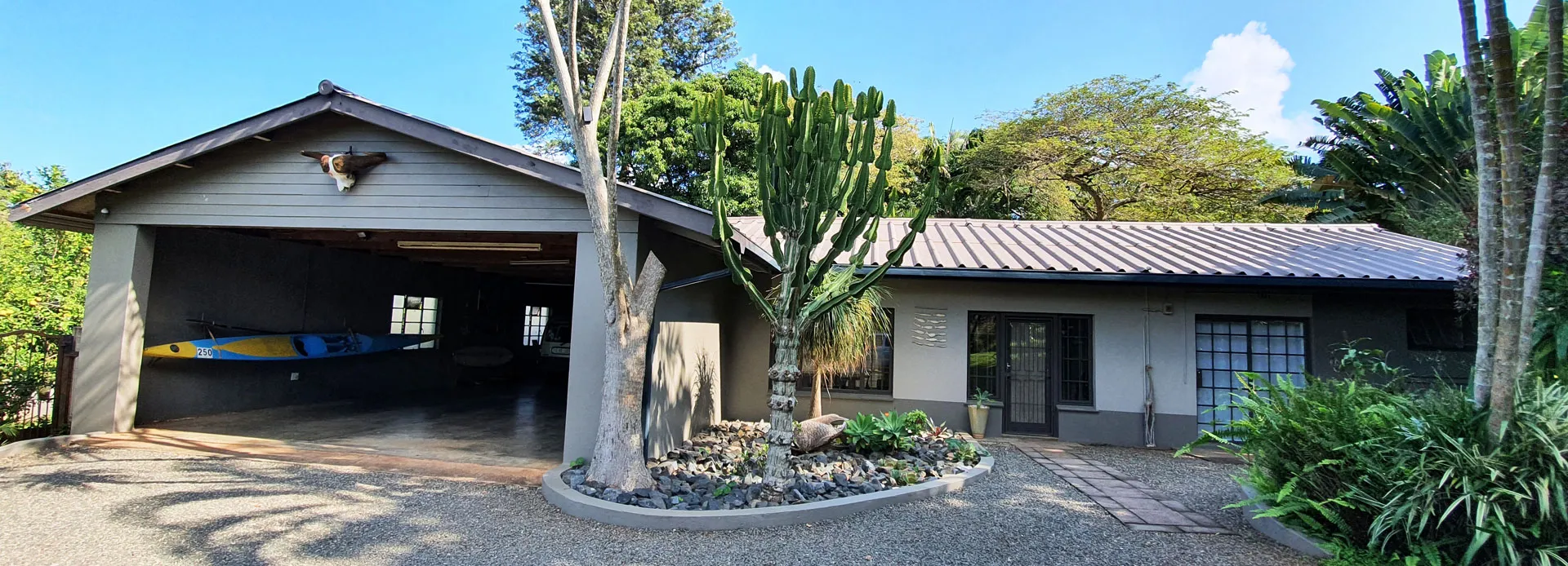 Singlestory house with a carport plants and gravel driveway in a sunny setting