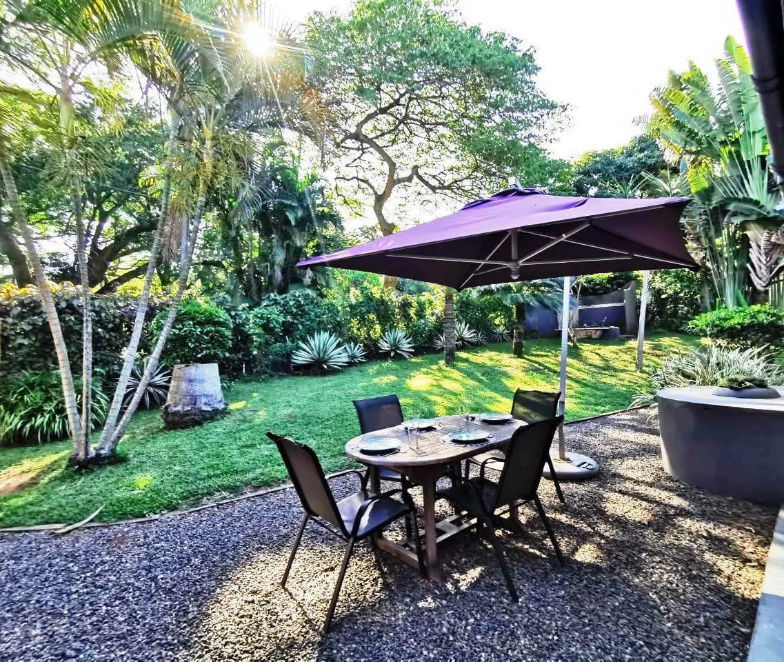 Outdoor dining area with table chairs and umbrella in a lush garden