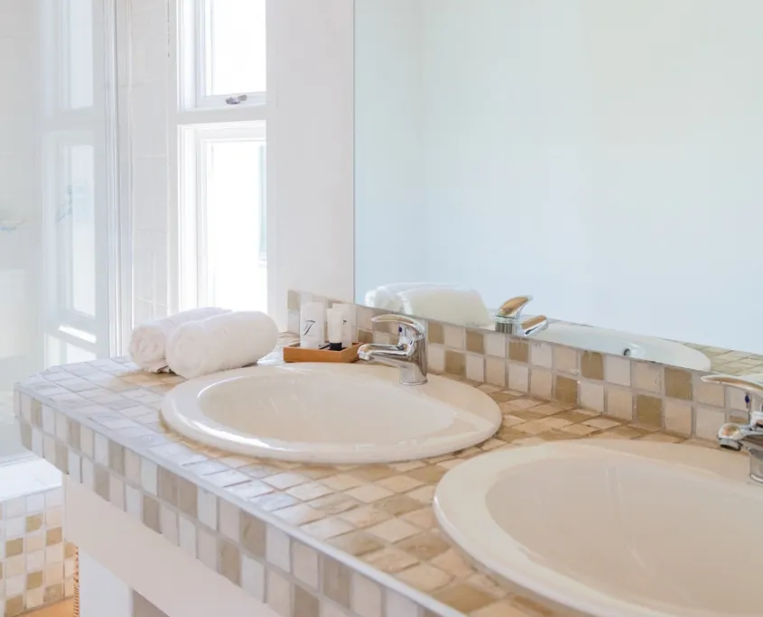 Two white sinks with a tiled backsplash in a bright bathroom