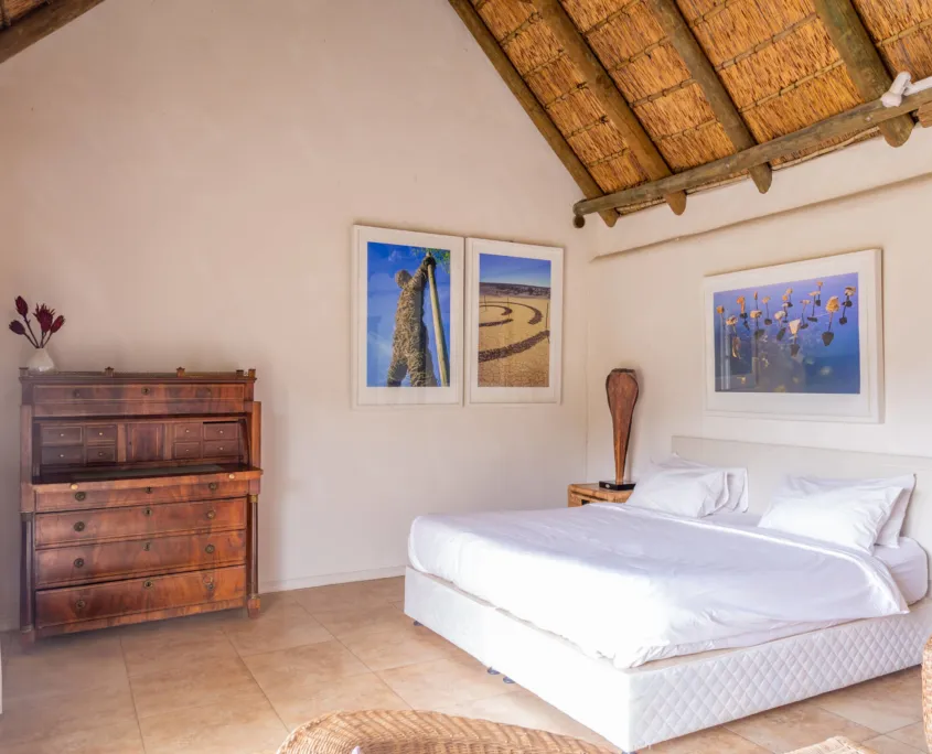 Bedroom with a large bed wooden dresser and thatched ceiling featuring nature artwork