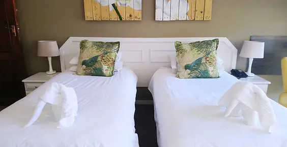 Two neatly made beds with decorative pillows and towel swans in a bedroom