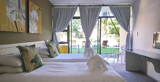 Two beds in a room with patterned curtains and a garden view
