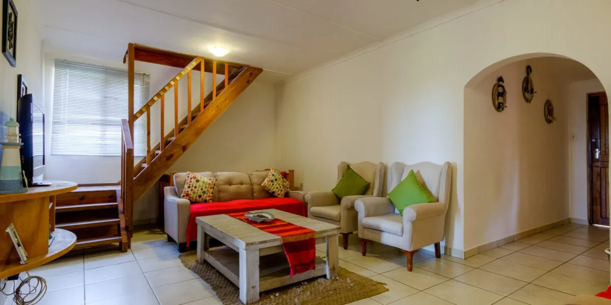 Living room with staircase sofa armchairs and coffee table on tiled floor