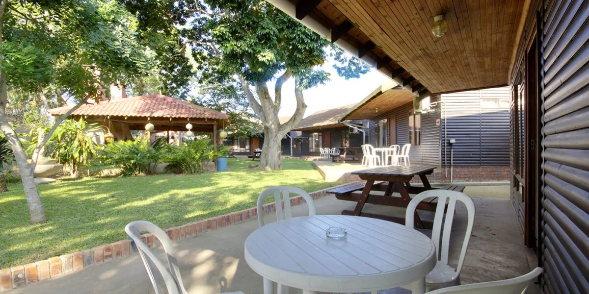 Outdoor seating area with white chairs and tables near a grassy lawn and buildings