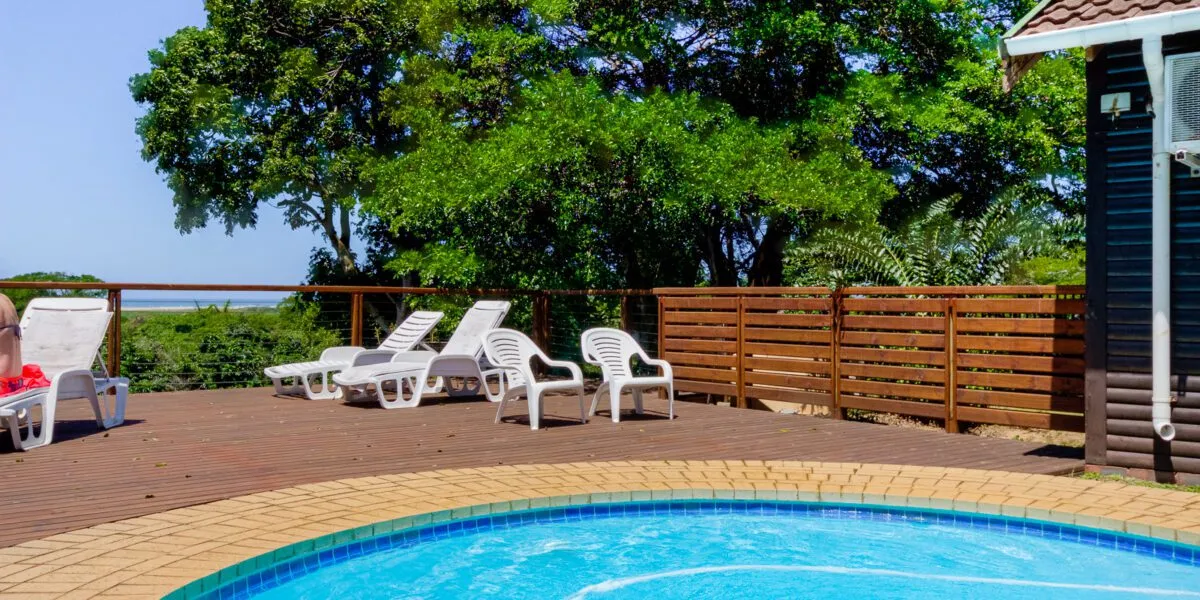 Wooden deck with lounge chairs pool and trees in the background