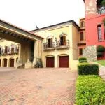 Large colorful building with red doors and balconies brick driveway and greenery