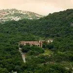 A building nestled in a lush green forested valley with hills in the background
