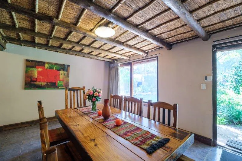Wooden dining table with chairs in a rustic room with thatched ceiling