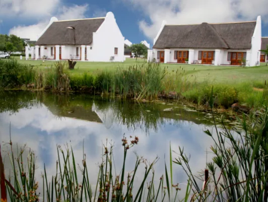 White cottages with thatched roofs by a pond surrounded by greenery