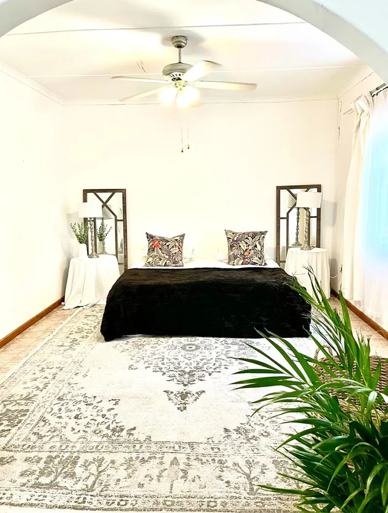 Bedroom with black bed white walls ceiling fan and patterned rug